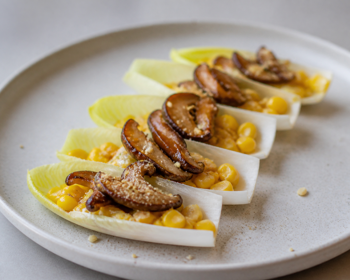 Endive veggie shells with warm sweet corn and mild miso cream, glazed shiitake, and crunchy sunflower dust