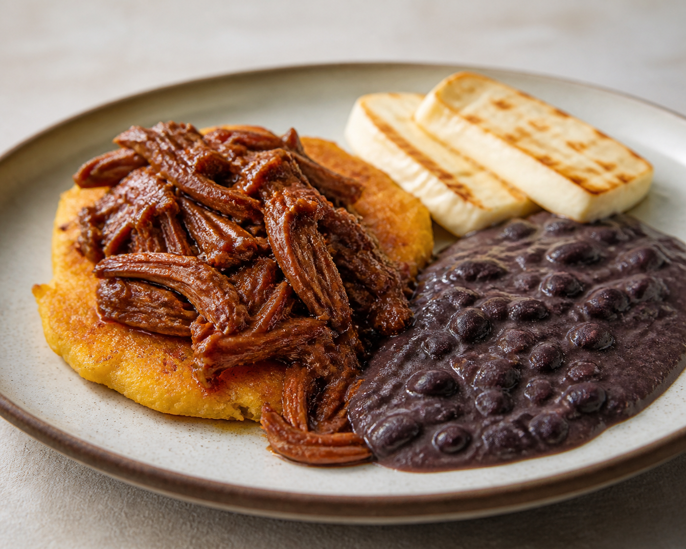 Caracas-Style Hominy and Green Plantain Cakes with Shredded Beef in Panela Glaze, Creamy Black Beans, and Seared White Cheese