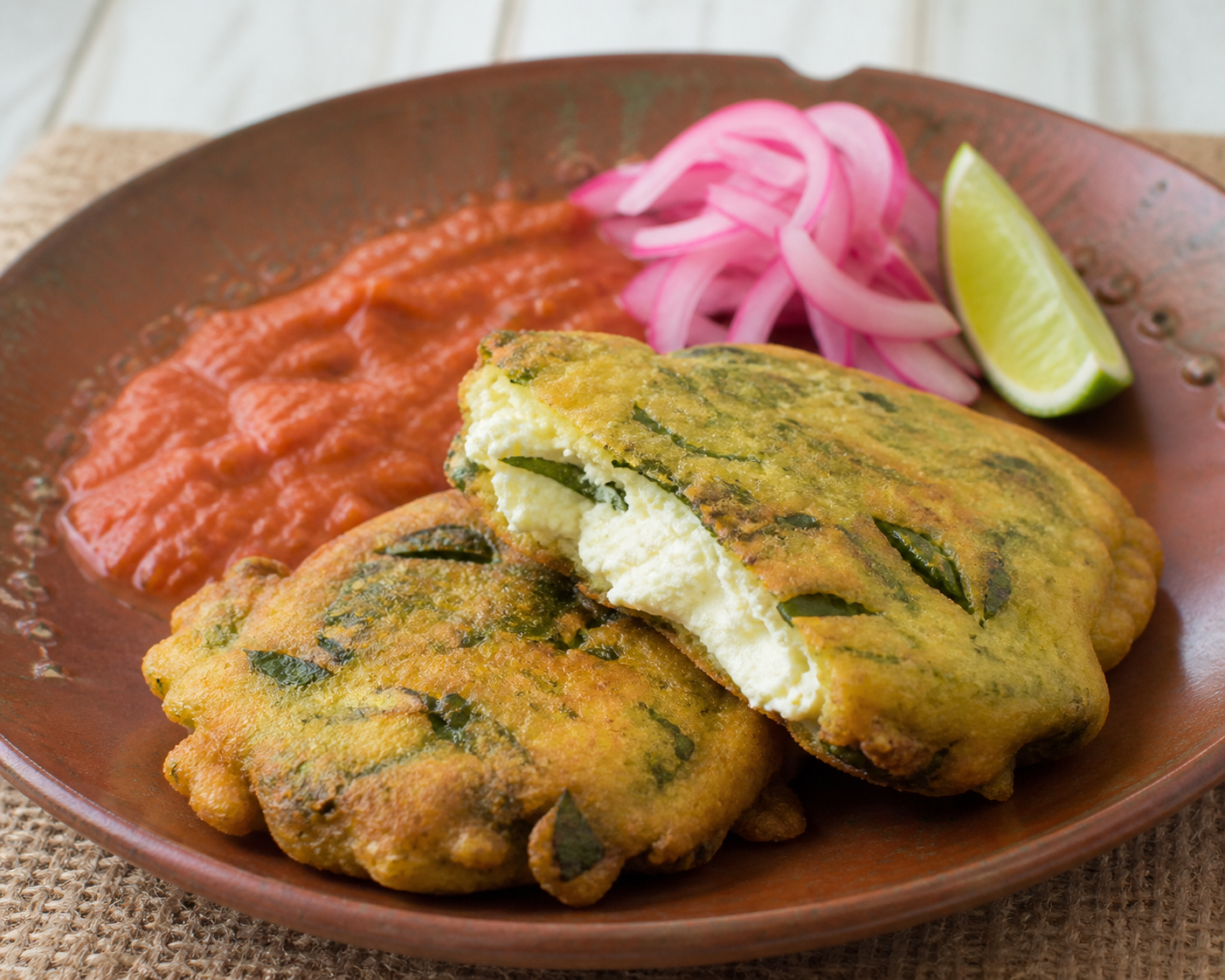 Tortitas salvadoreñas de plátano verde y chipilín con relleno de cuajada, salsa de tomate asado y cebolla curtida al limón